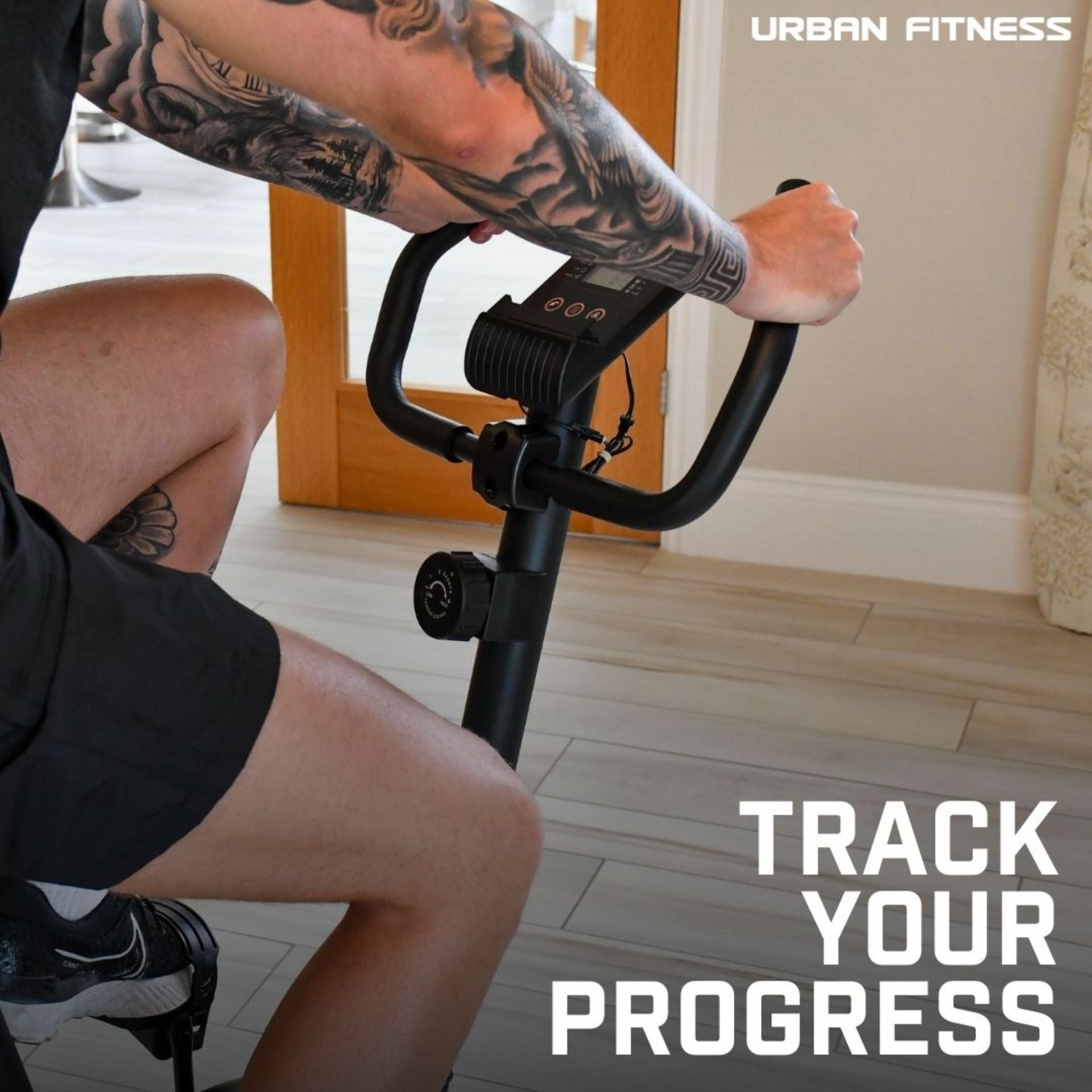 A person with tattooed arms pedals the Urban Fitness Magnetic Exercise Bike indoors. "Urban Fitness" and "Track Your Progress" appear, showcasing adjustable resistance for a personalized home cardio workout.