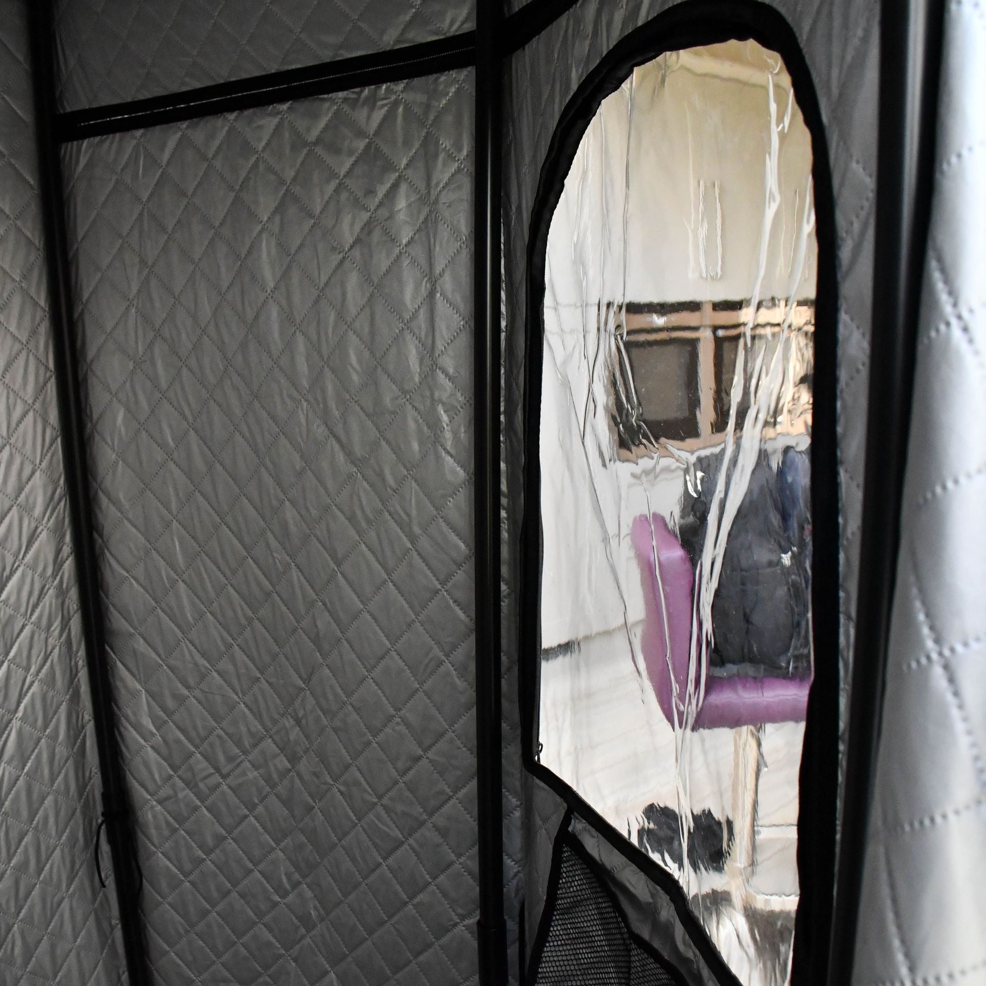 The Urban Fitness Recovery Home Sauna by Urban Fitness is a quilted, silver portable steam sauna with a zippered clear window, shown in a room with a purple chair, desk, and items on the chair.