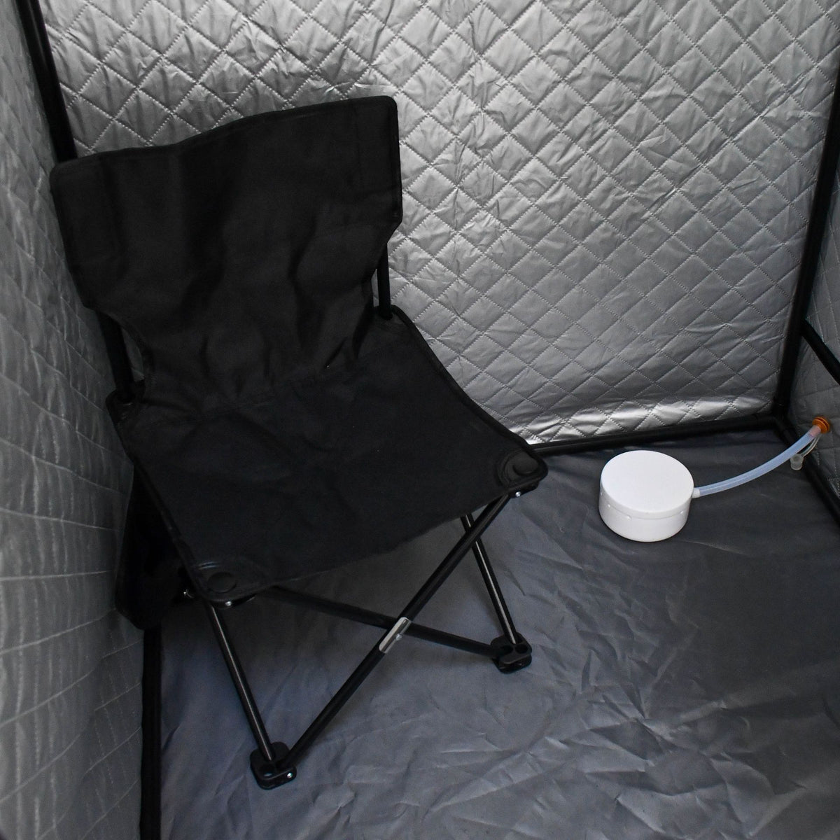 An Urban Fitness Recovery Home Sauna by Urban Fitness features quilted silver-gray walls and floor, a black folding chair inside, and includes a round white heat therapy device attached by a thin tube.