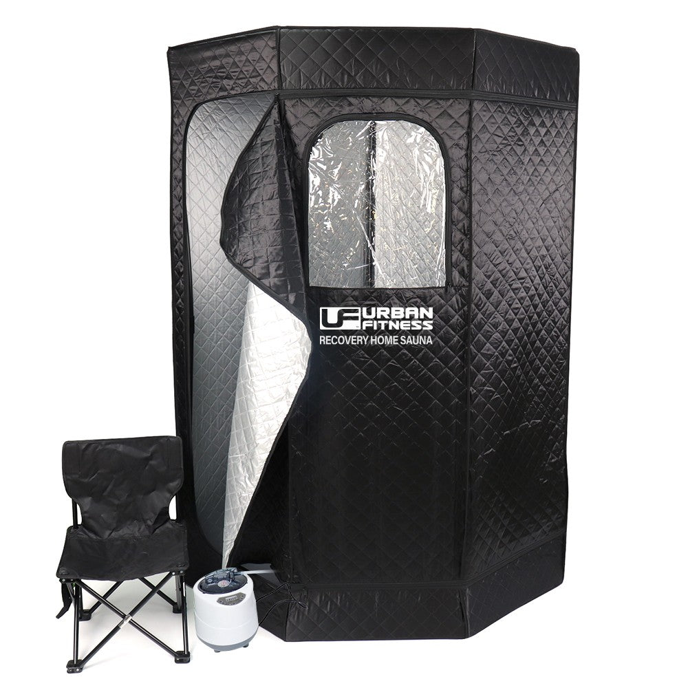 The Urban Fitness Recovery Home Sauna is a black quilted portable tent with a partially open zippered door and reflective interior, branded with Urban Fitness. A foldable black chair and white steam generator are included for heat therapy.