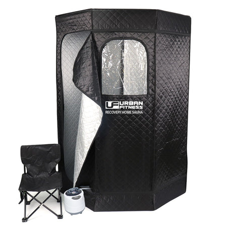 The Urban Fitness Recovery Home Sauna is a black quilted portable tent with a partially open zippered door and reflective interior, branded with Urban Fitness. A foldable black chair and white steam generator are included for heat therapy.