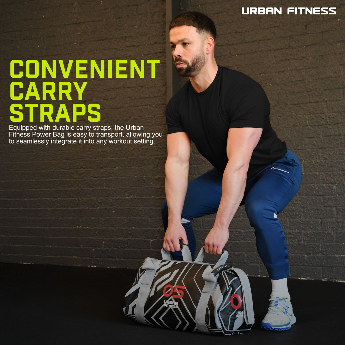 A man in a black t-shirt and blue pants squats while gripping an Urban Fitness Power Bag. The bag’s visible carry straps ensure easy transport, making it ideal for full-body conditioning. Brand: Urban Fitness.