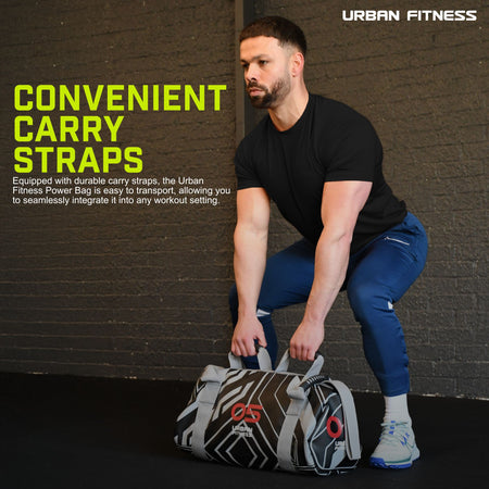 A man in a black t-shirt and blue pants squats while gripping an Urban Fitness Power Bag. The bag’s visible carry straps ensure easy transport, making it ideal for full-body conditioning. Brand: Urban Fitness.