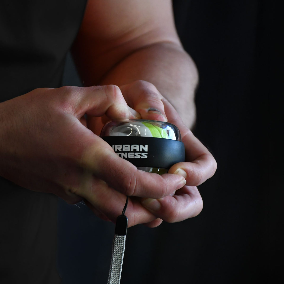 A person holds an Urban Fitness Wrist Exerciser Ball with a black and transparent design, featuring a grip strength–enhancing gyro and wrist strap, by Urban Fitness, set against a dark background.