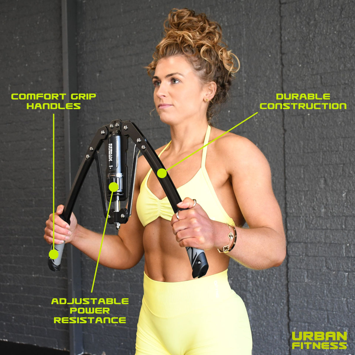 A woman in a yellow workout outfit uses the Urban Fitness Hydraulic Arms Trainer, featuring comfort grip handles, adjustable resistance, and durable construction. "Urban Fitness" appears in the bottom right corner.