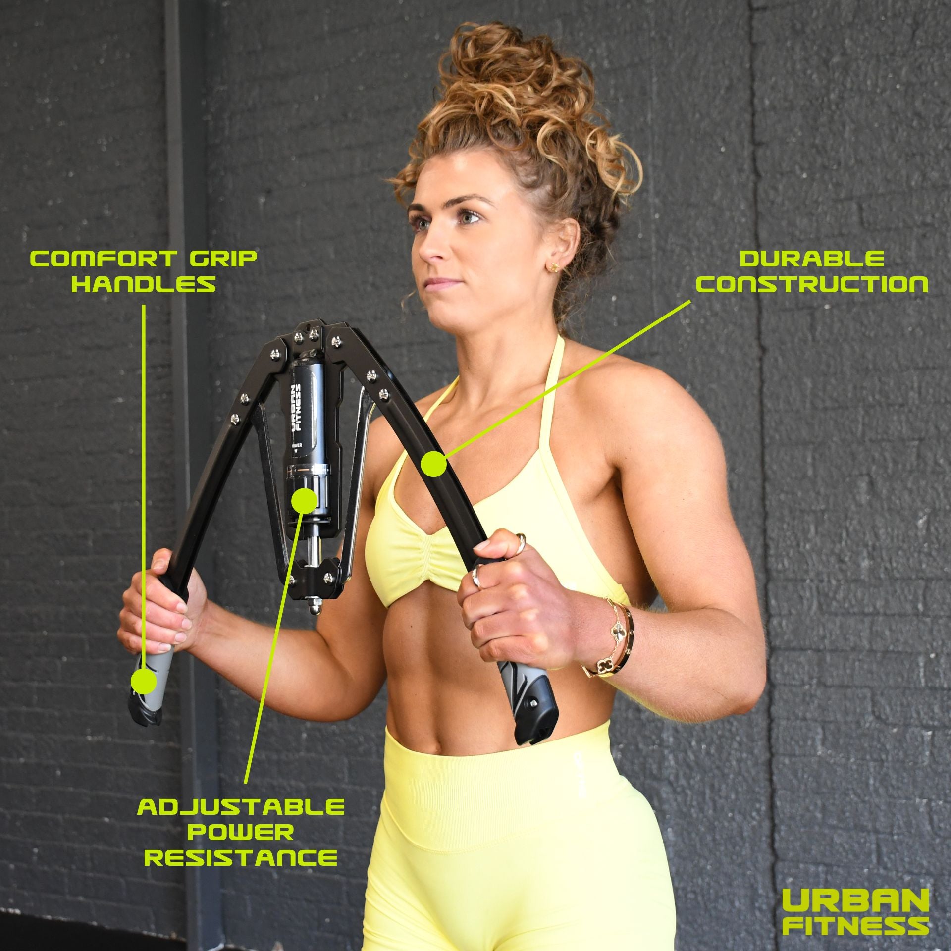A woman in a yellow workout outfit uses the Urban Fitness Hydraulic Arms Trainer, featuring comfort grip handles, adjustable resistance, and durable construction. "Urban Fitness" appears in the bottom right corner.