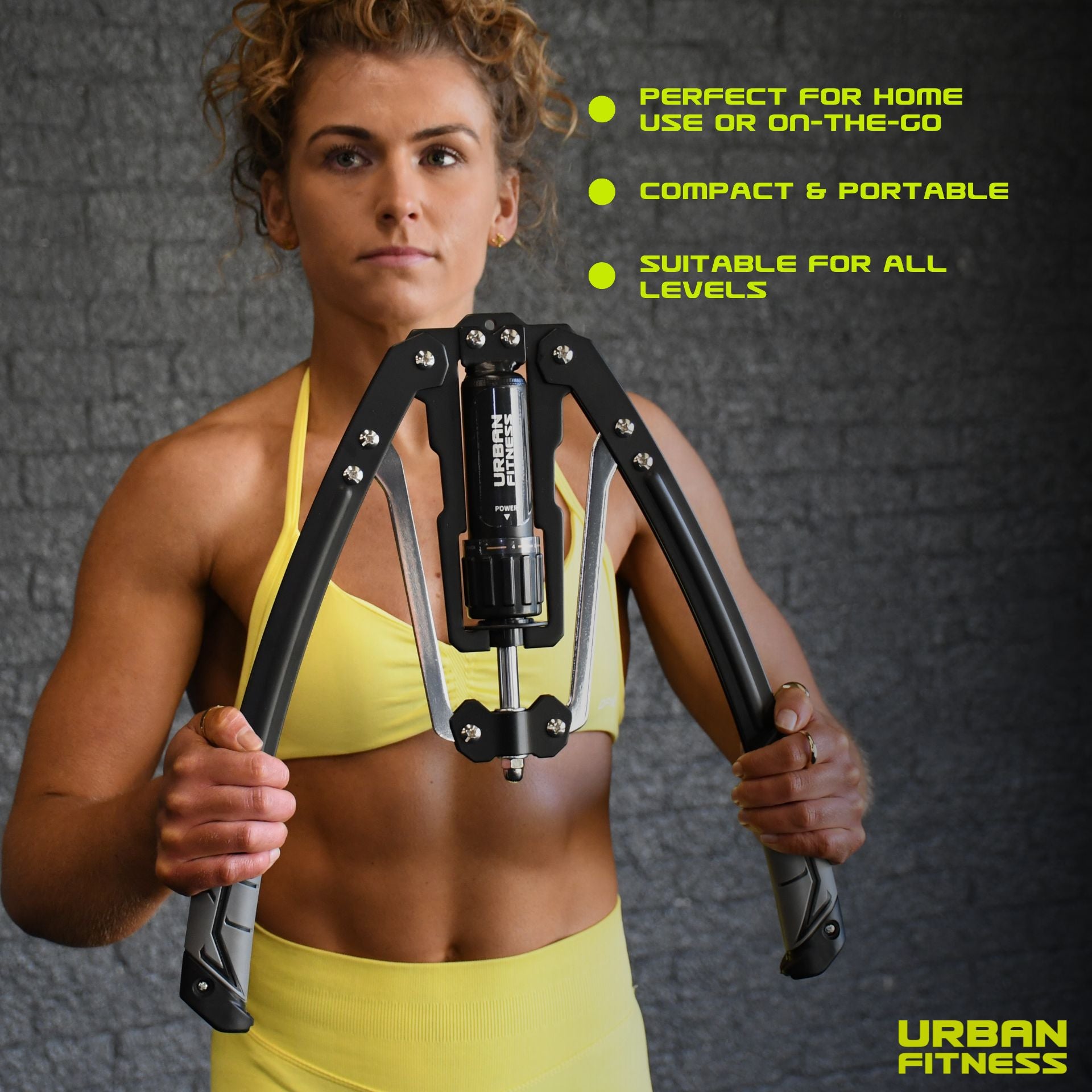 A woman in a yellow sports outfit holds the Urban Fitness Hydraulic Arms Trainer, a compact, portable exerciser with adjustable resistance—ideal for building upper body strength at home or on the go. URBAN FITNESS logo is visible in the corner.