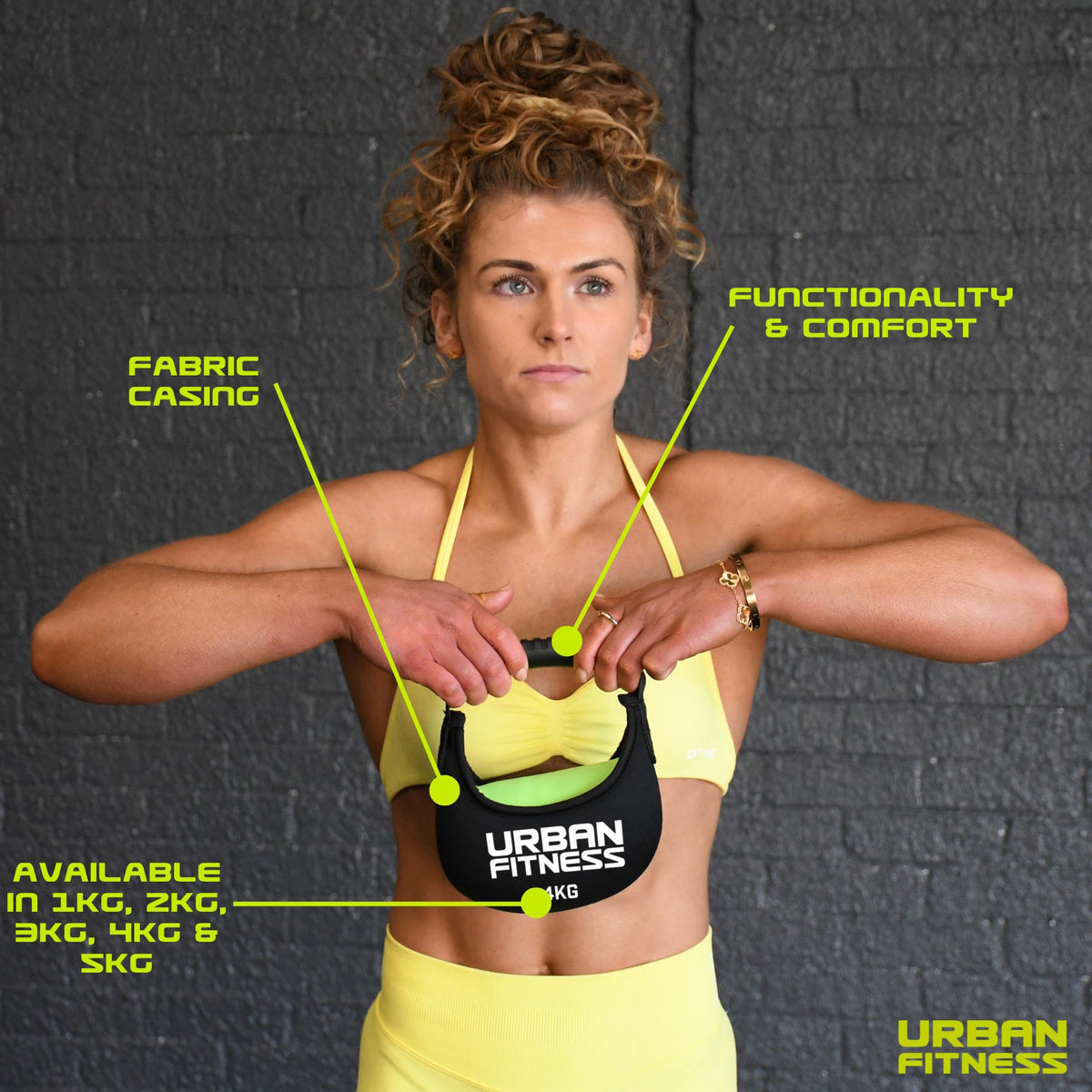 A woman in yellow fitness wear holds the Urban Fitness Fabric Kettlebell, featuring a soft fabric casing for comfort and functionality. Available in 1kg–5kg weights, it’s ideal for home gyms against a stylish gray brick wall backdrop.