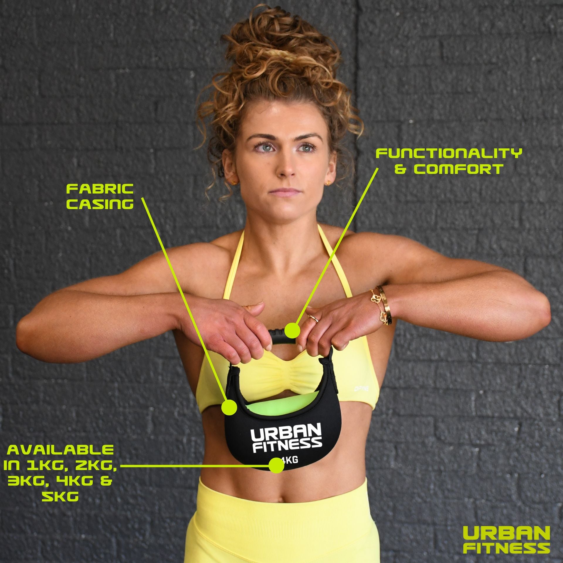 A woman in yellow fitness wear holds the Urban Fitness Fabric Kettlebell, featuring a soft fabric casing for comfort and functionality. Available in 1kg–5kg weights, it’s ideal for home gyms against a stylish gray brick wall backdrop.