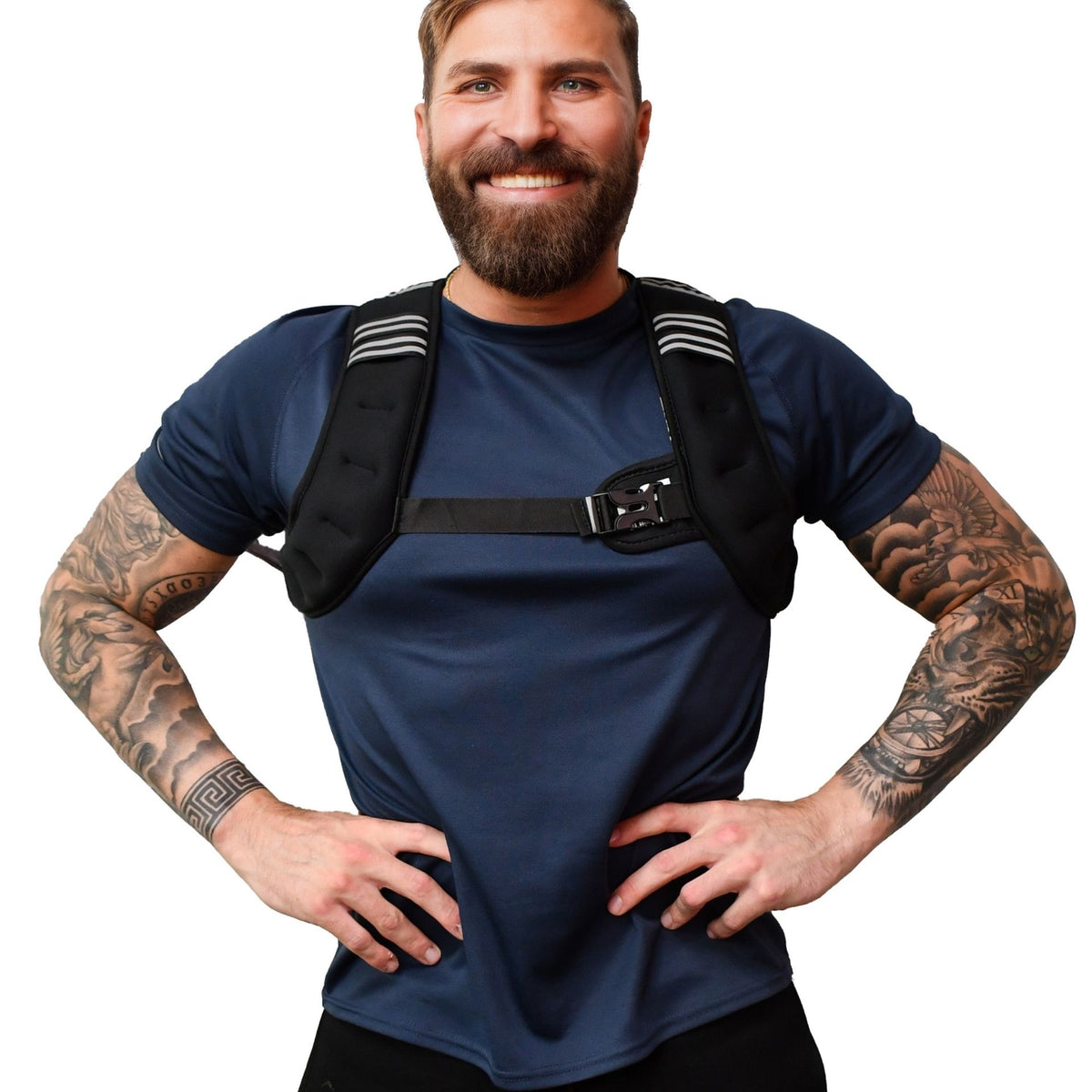 A smiling bearded man with tattooed arms stands hands on hips against a white background, wearing a navy shirt and the black Urban Fitness X Shape Weighted Vest by Urban Fitness, featuring striped shoulder pads.