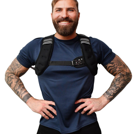 A smiling bearded man with tattooed arms stands hands on hips against a white background, wearing a navy shirt and the black Urban Fitness X Shape Weighted Vest by Urban Fitness, featuring striped shoulder pads.