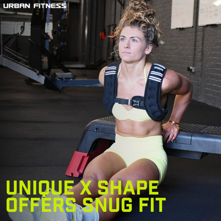 A woman in yellow sportswear sits on the gym floor, resting after strength training with the Urban Fitness X Shape Weighted Vest. Text: UNIQUE X SHAPE OFFERS SNUG FIT. Urban Fitness logo appears in the top left corner.