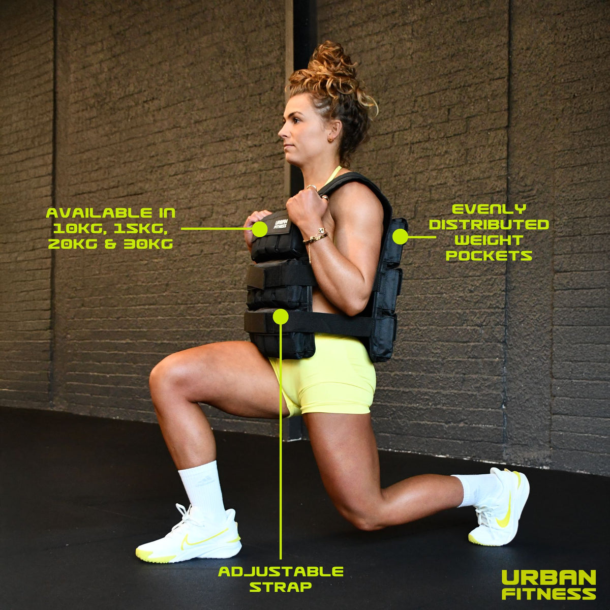 A woman in a gym performs a lunge wearing the black Urban Fitness Adjustable Weighted Vest. Labels show adjustable straps, evenly distributed weight pockets for progressive overload, and available weights: 10kg, 15kg, 20kg, 30kg. Urban Fitness logo appears.