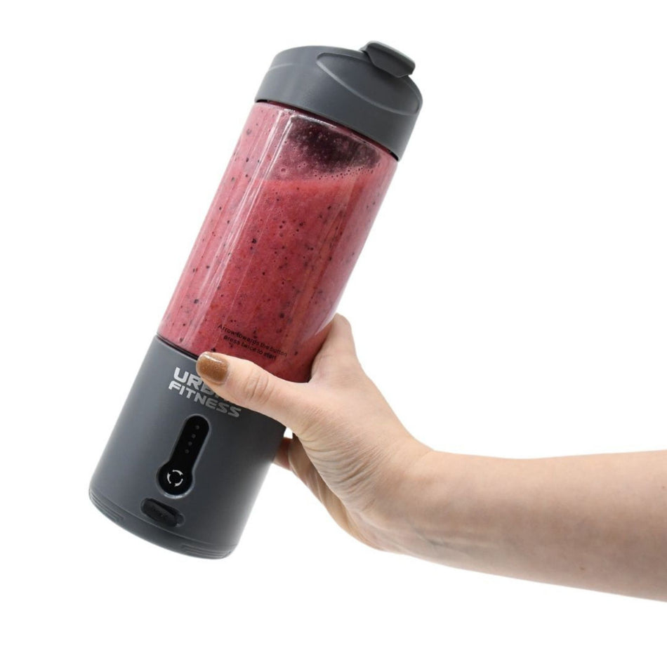 A hand holds the Urban Fitness VitalFuse Portable Blender filled with a red and purple smoothie, "Urban Fitness" on the side—an ideal portable blender bottle for on-the-go nutrition—set against a plain white background.