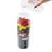 A hand pours water from a glass jug into the Urban Fitness VitalFuse Portable Blender filled with raspberries, mango, blueberries, bananas, and strawberries—an ideal on-the-go nutrition solution from Urban Fitness.