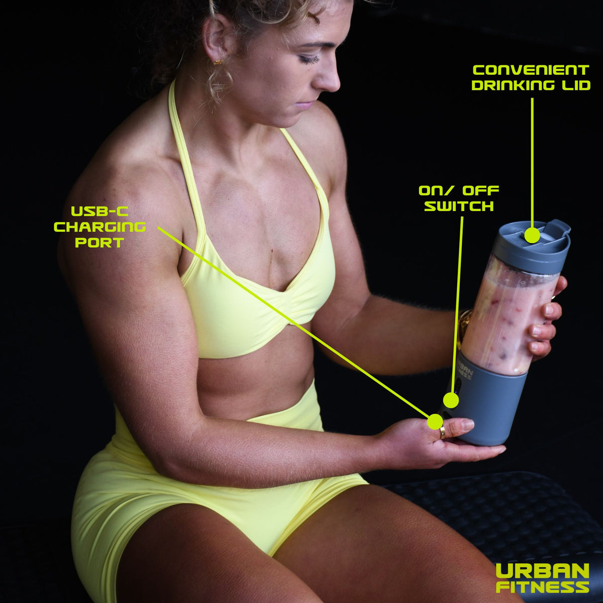 A woman in yellow sportswear holds the Urban Fitness VitalFuse Portable Blender, with labels showing its USB-C charging port, on/off switch, convenient drinking lid, and Urban Fitness logo—ideal for active lifestyles and nutrition on the go.