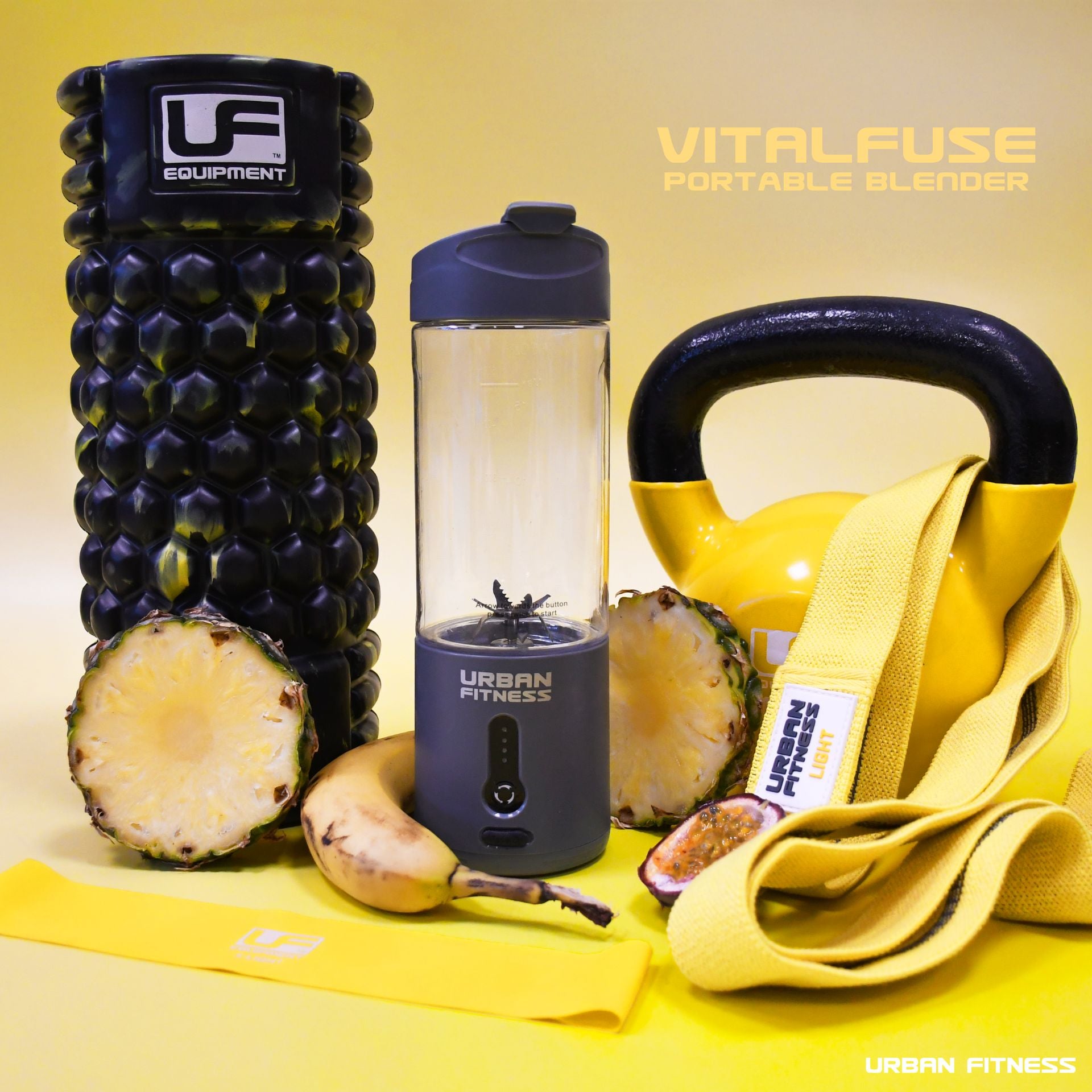 A black foam roller, yellow kettlebell, resistance band, half a pineapple, banana, fitness cards, and the Urban Fitness VitalFuse Portable Blender with fruit inside are arranged on yellow—ideal for on-the-go nutrition. Text: Urban Fitness.