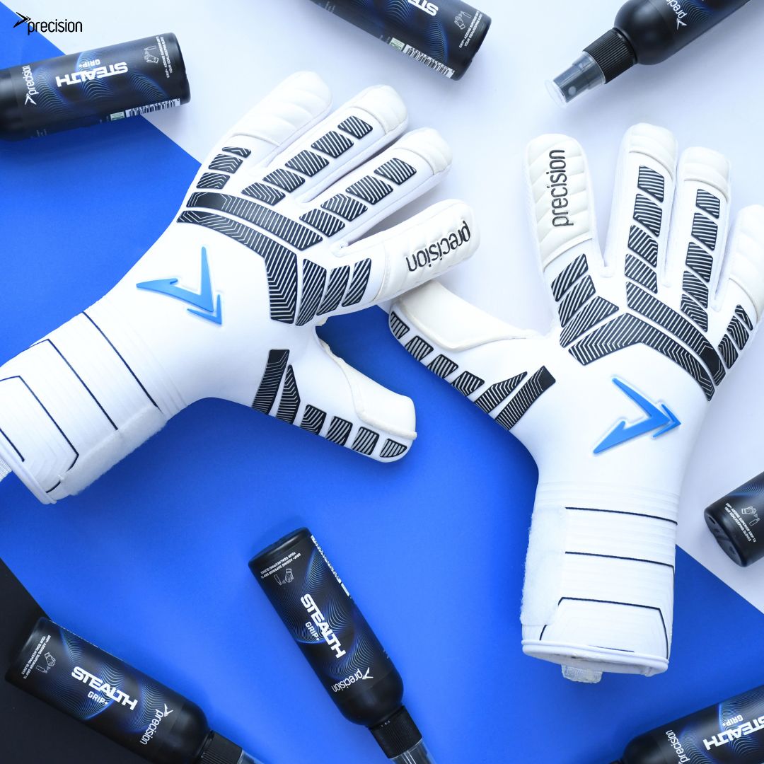 A pair of Precision Elite 3.0 Contact Goalkeeper Gloves by Martin Berrill Sports in white and blue with black accents, displayed with Stealth spray bottles on a blue and white background. The “precision” logo is visible on the gloves and corner.