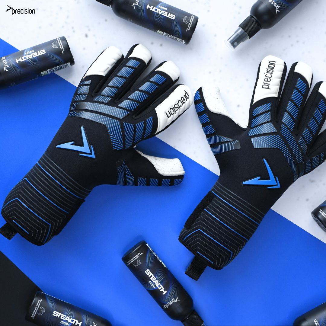A pair of Precision Training Elite 3.0 Quartz Goalkeeper Gloves in black and blue are shown on a blue and white surface, surrounded by Stealth sports spray bottles to enhance grip.