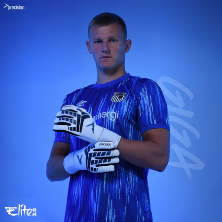 A male soccer player in a blue patterned jersey and Precision Training's Elite 3.0 Giga Goalkeeper Gloves stands confidently against a blue background, looking at the camera. "Elite" and "Precision" appear in the corners, showcasing his elite grip.