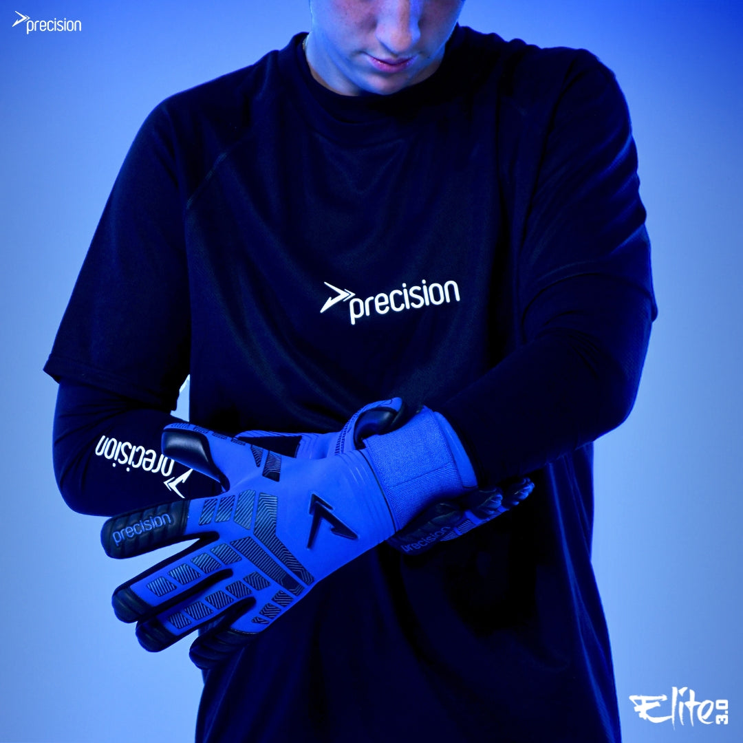 A person in a black Precision Training sports shirt puts on blue and black Precision Elite 3.0 Grip Goalkeeper Gloves, featuring elite grip, against a blue background. The Precision Training and Elite Sport logos are visible.