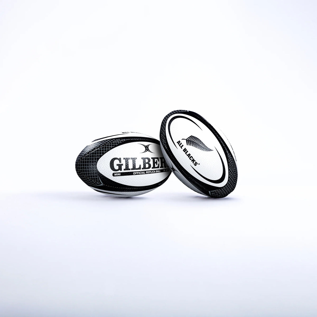 Two black and white Gilbert rugby balls are shown on a white background. One is the Gilbert All Blacks Replica Rugby Ball Mini, featuring the iconic silver fern—ideal for New Zealand rugby fans.