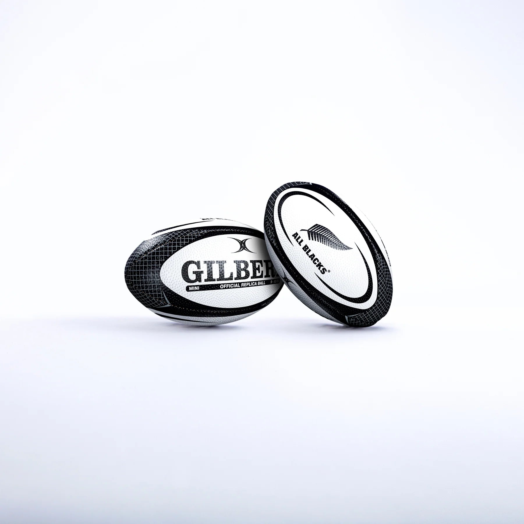 Two black and white Gilbert rugby balls are shown on a white background. One is the Gilbert All Blacks Replica Rugby Ball Mini, featuring the iconic silver fern—ideal for New Zealand rugby fans.