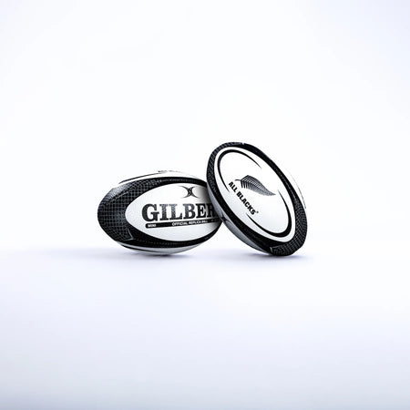 Two black and white Gilbert rugby balls are shown on a white background. One is the Gilbert All Blacks Replica Rugby Ball Mini, featuring the iconic silver fern—ideal for New Zealand rugby fans.