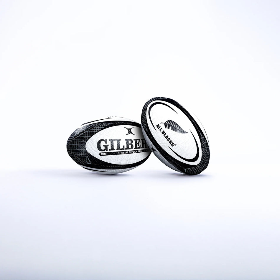 Two black and white Gilbert rugby balls are shown on a white background. One is the Gilbert All Blacks Replica Rugby Ball Mini, featuring the iconic silver fern—ideal for New Zealand rugby fans.