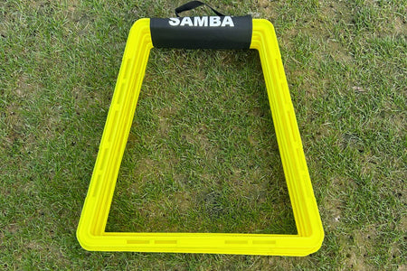 A yellow, trapezoid-shaped Samba Pro Agility Trapeze Set by Samba Sports with a black handle rests on green grass, perfect for speed and coordination training.