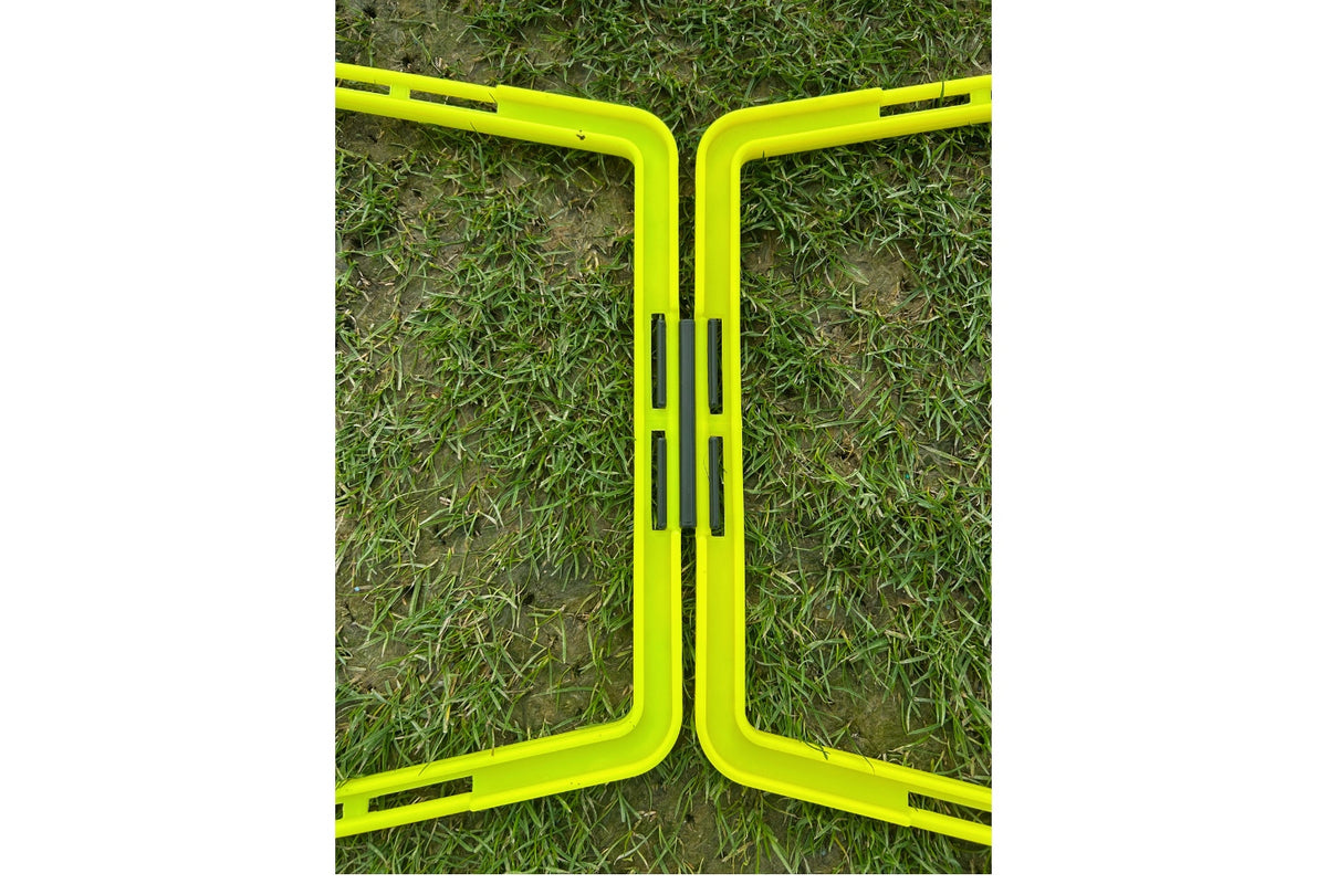 Two yellow plastic frames with black hinges, part of the Samba Pro Agility Trapeze Set by Samba Sports, form a zigzag on grass—ideal for speed and coordination drills, even on short or patchy lawns.