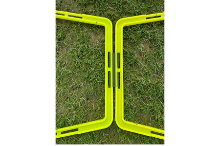 Two yellow plastic frames with black hinges, part of the Samba Pro Agility Trapeze Set by Samba Sports, form a zigzag on grass—ideal for speed and coordination drills, even on short or patchy lawns.