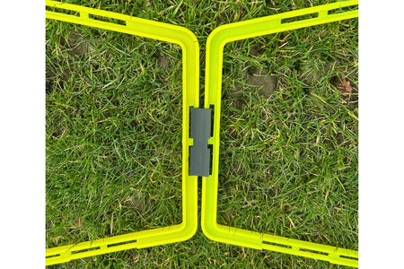 Two bright yellow Samba Sports Pro Agility Trapeze Set frames, joined by a dark gray hinge, rest on green grass in a zigzag shape—an ideal portable training aid for agility drills.