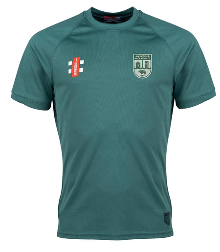 The green Alvington & Woolaston Matrix V2 T-Shirt by Gray Nicolls features short sleeves, moisture-wicking fabric, a shield badge with text on the left chest, and a white plus sign with an orange bar on the right chest. Displayed on a plain white background.