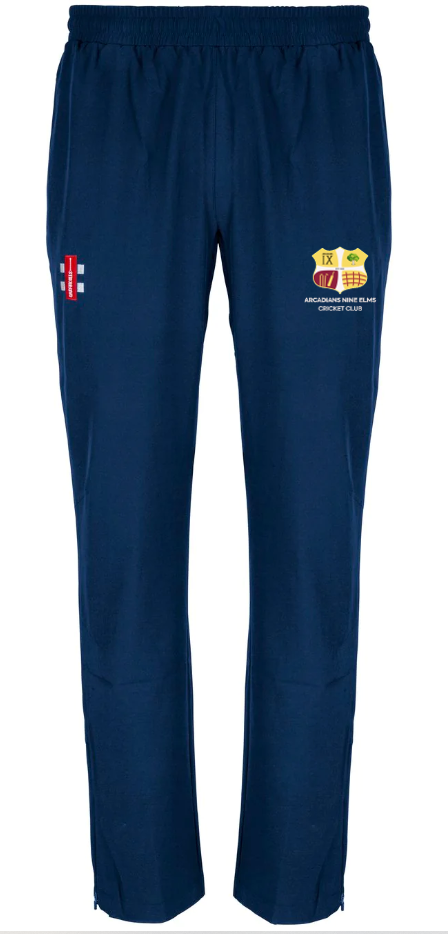 The Gray Nicolls Arcadians Nine Elms CC Velocity Track Trousers are navy blue with an elastic waistband, a red and white logo on the left thigh, and a yellow-red crest with text on the right—ideal for cricket training.