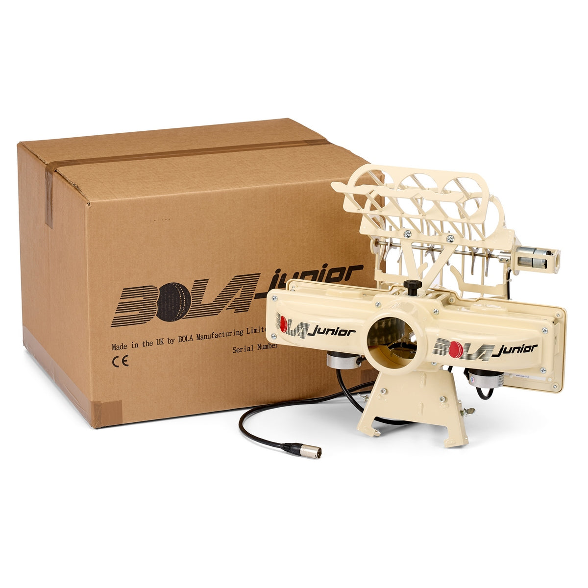 The Bola BOLA Junior Bowling Machine is pictured beside its shipping box. Designed for junior cricket practice, the cream-colored machine from Bola features dual throwing wheels and a ball feeder attachment on top, with a visible power cable.