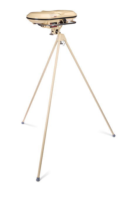 A beige tripod-mounted device with a circular top, reminiscent of a vintage electronic instrument or appliance, stands on three long legs with rubber feet—evoking the iconic silhouette of the Bola Professional Bowling Machine by Bola, a celebrated tool widely used for cricket batting practice.