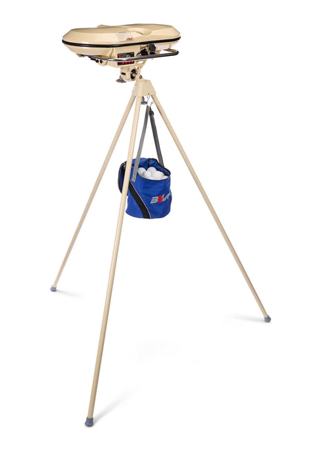 A beige Bola Professional Bowling Machine with a round top, mounted on a tall tripod stand, and a blue bucket of baseballs suspended from the center.