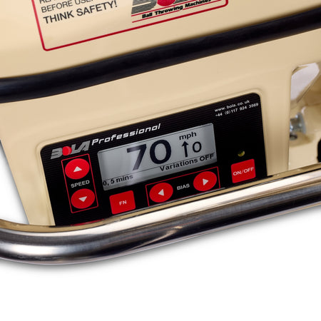 Here is a revised version of the sentence, incorporating the provided product data: Close-up of the Bola Professional Bowling Machine’s digital control panel by Bola, featuring an ePaper display showing a 70 mph speed for cricket batting practice, with red buttons below and a safety warning label above.