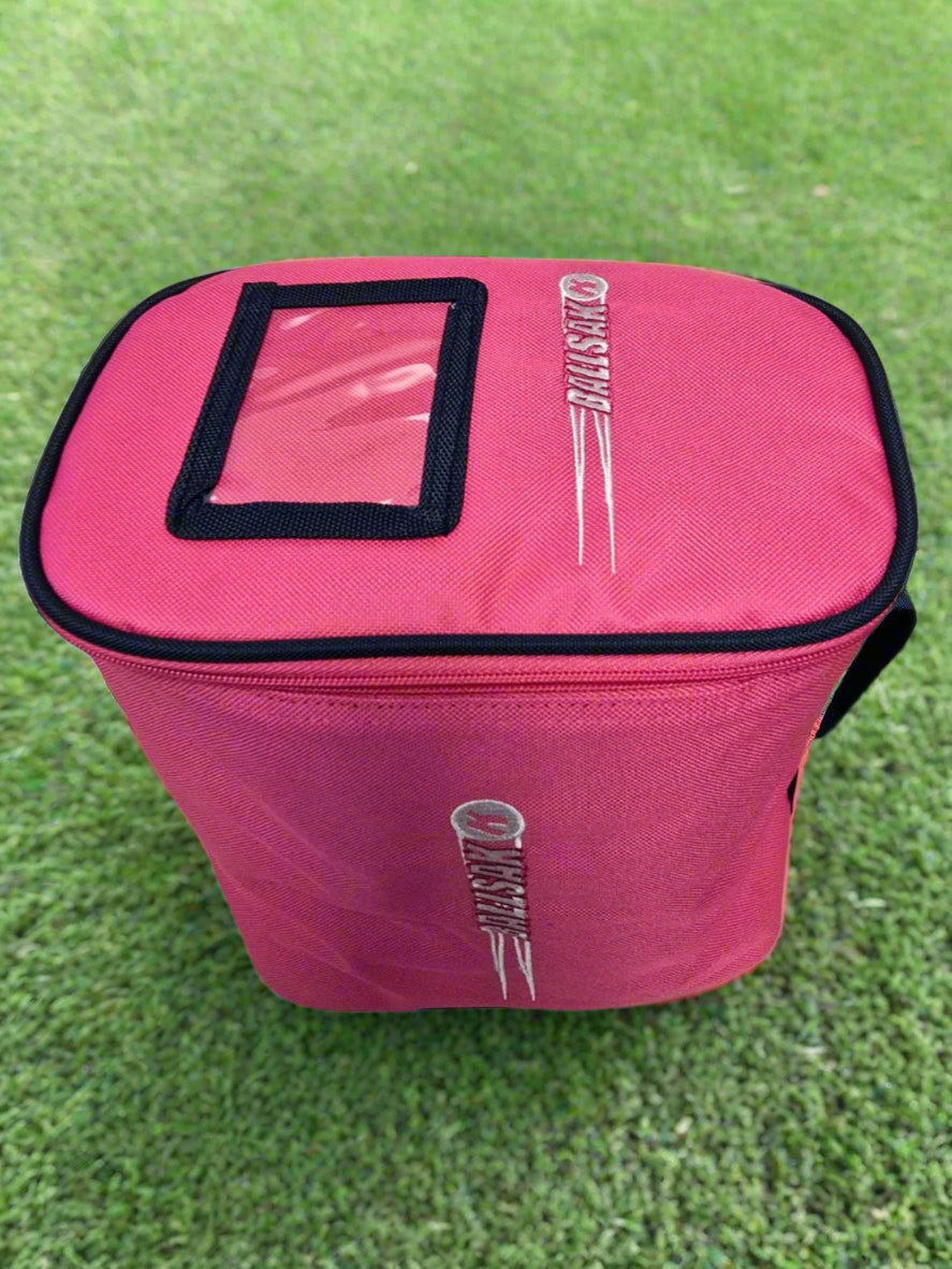 The Katchet BallSak by Katchet is a rectangular pink bag with a black-bordered clear window on top, shown on green grass. It features "CRICKET" and a ball logo on the sides—perfect for carrying cricket or hockey balls.