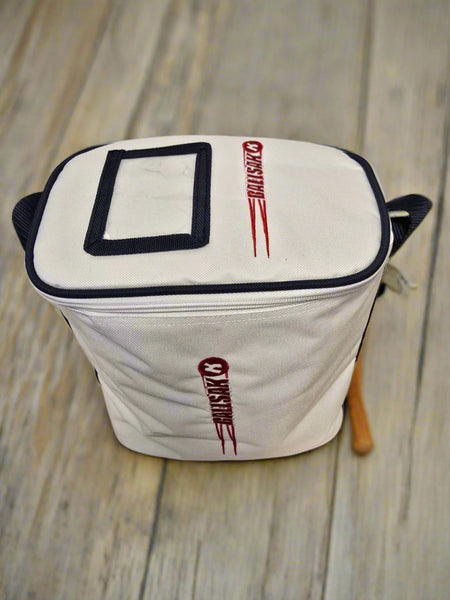 A white, rectangular Katchet BallSak by Katchet with black trim and two red MasterChef logos—one on top and one on the side—rests on a wooden surface. A wooden handle peeks out from the side. Ideal for stylishly storing hockey balls.