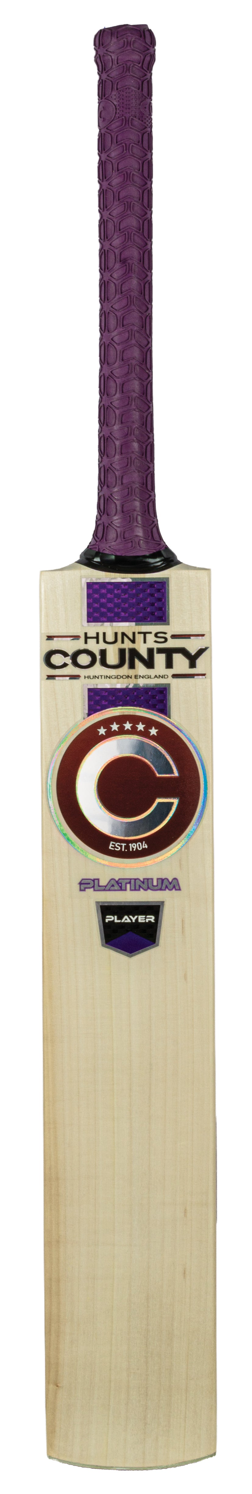 A Hunts County Platinum Players Junior Cricket Bat with a purple grip and country branding on the blade, featuring a large C logo and the word “PLATINUM” at the bottom.