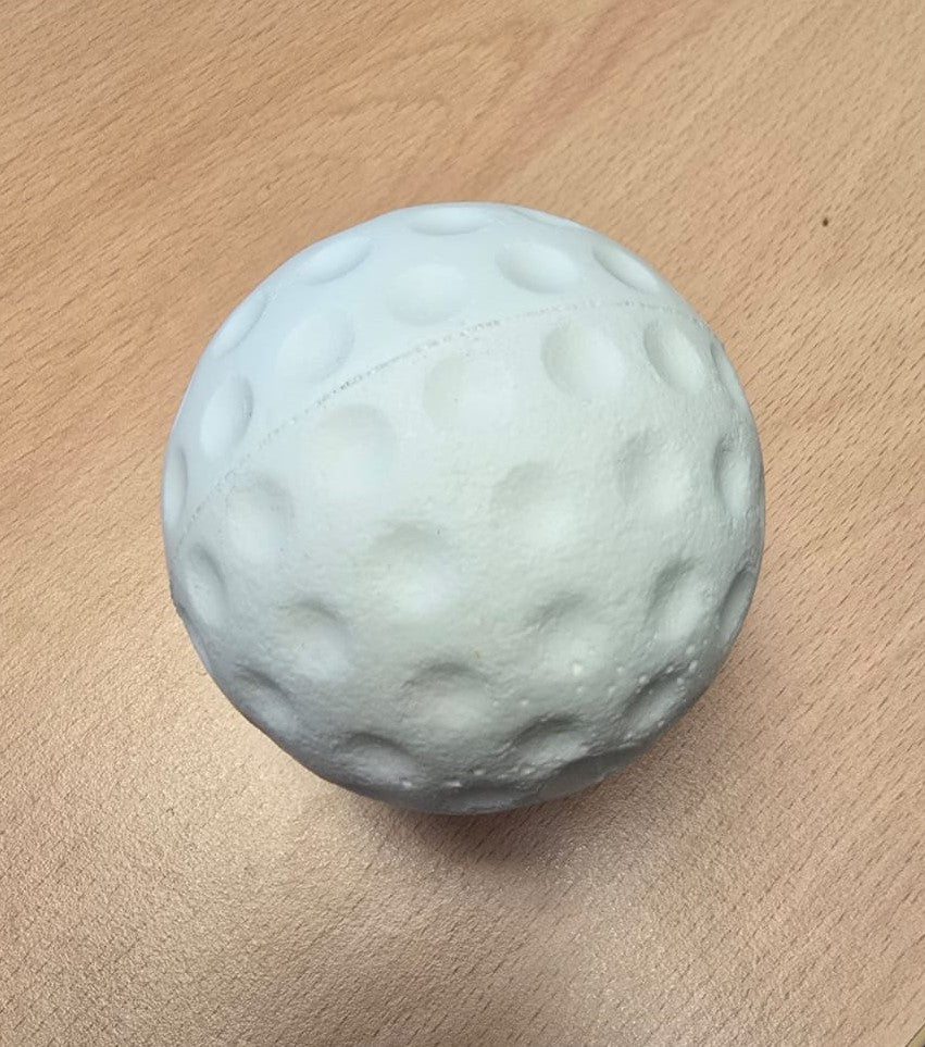 A white, dimpled, ball-shaped object resembling a golf ball sits on a light wooden surface, similar to Bola Senior Bowling Machine Practice Balls (White) by Bola.