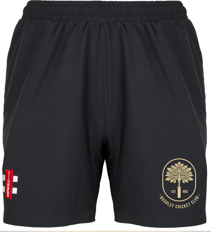 The Gray Nicolls Bushley CC Ladies Velocity Shorts feature the club logo in gold on the right leg, a red and white patch on the left leg, and have an elastic waistband without a visible drawstring.