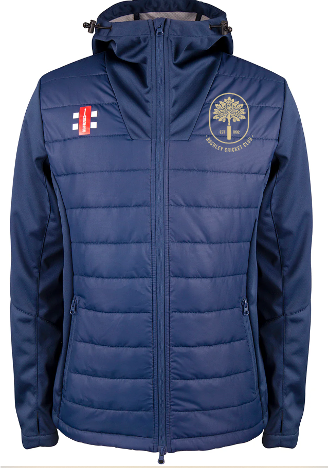 The Bushley CC Pro Performance Full Zip Jacket by Gray Nicolls is blue, features a hood, front zipper, two side pockets, and has two chest logos: a red and white emblem on the left and CRANLEIGH CRICKET CLUB yellow tree crest on the right.