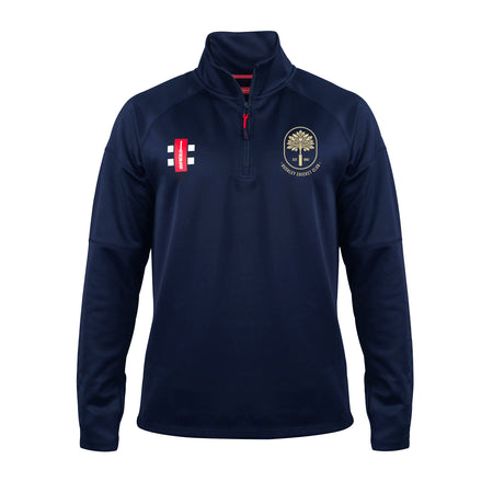 The Gray Nicolls Bushley CC Pro Thermo Fleece is a navy blue long-sleeve 1/4 zip pullover with raglan sleeves, a cricket bat and ball logo on the left chest, and a gold tree emblem with text on the right chest.