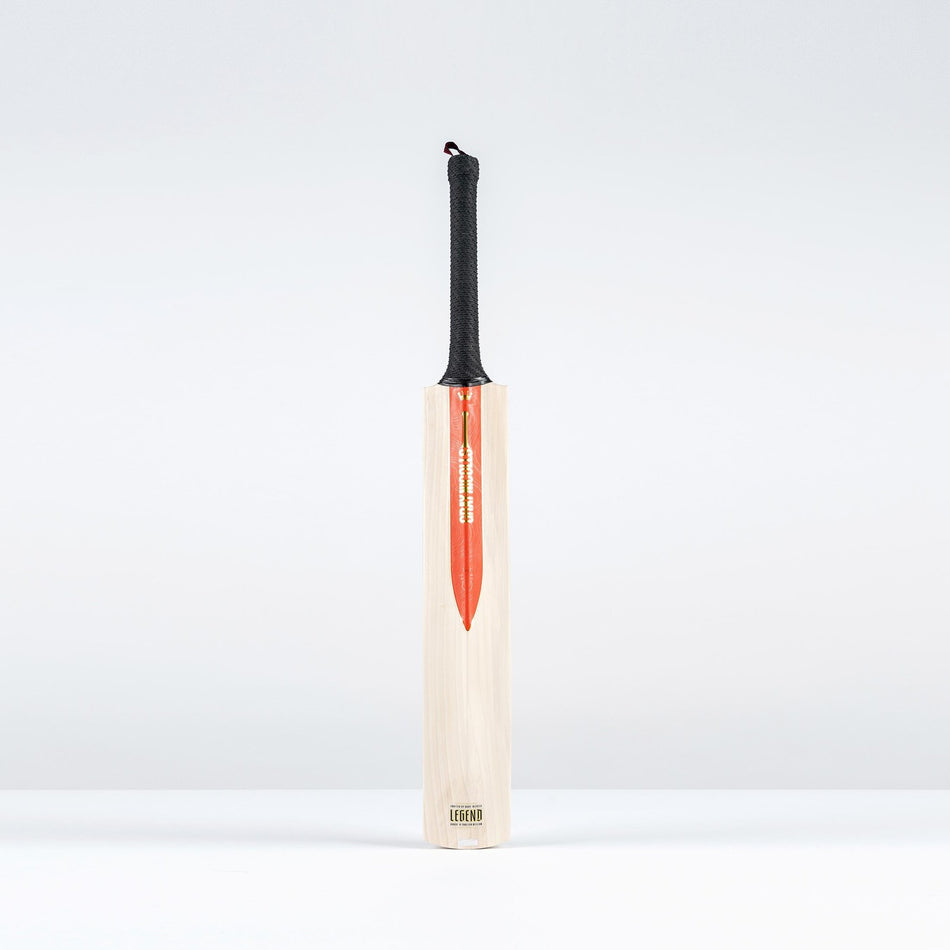 The Gray Nicolls Legend Gold Edition SH Cricket Bat, crafted from premium English willow, features a black grip and red blade design. It stands upright against a plain background, showcasing its expanded sweet spot.