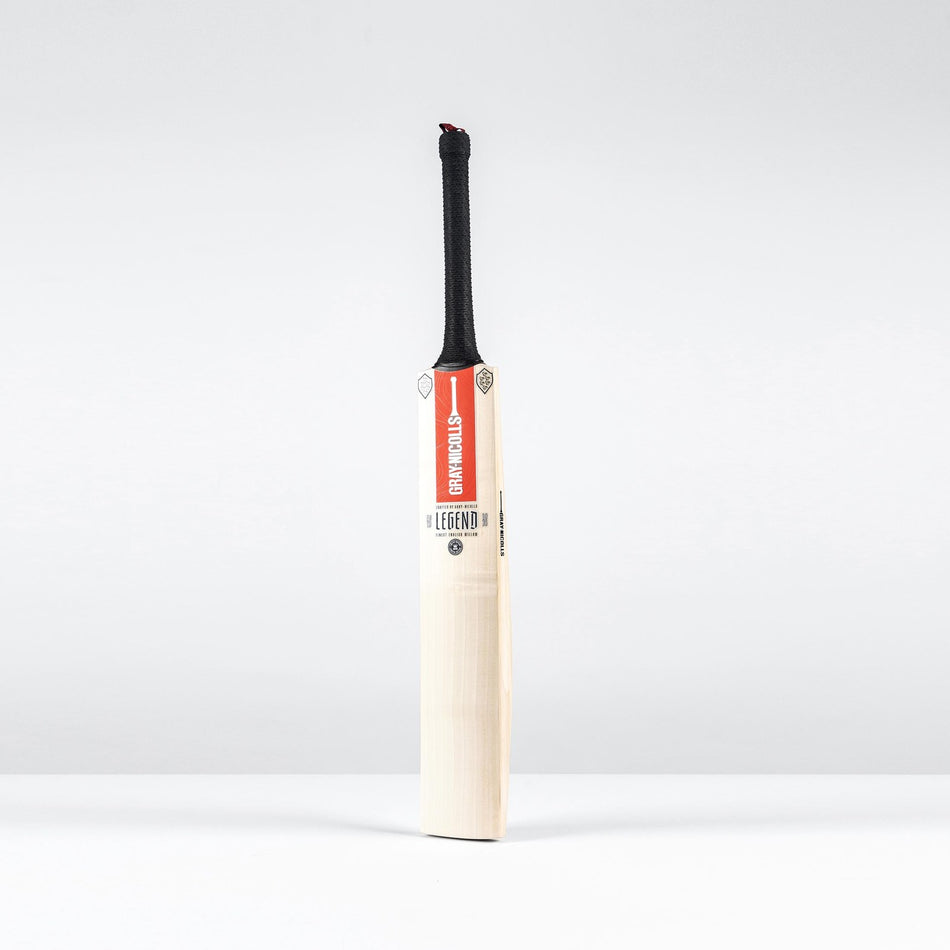 The Gray Nicolls Legend Silver Edition SH Cricket Bat, featuring a black grip, red label on the upper front, and expanded sweet spot, stands upright against a plain white background.