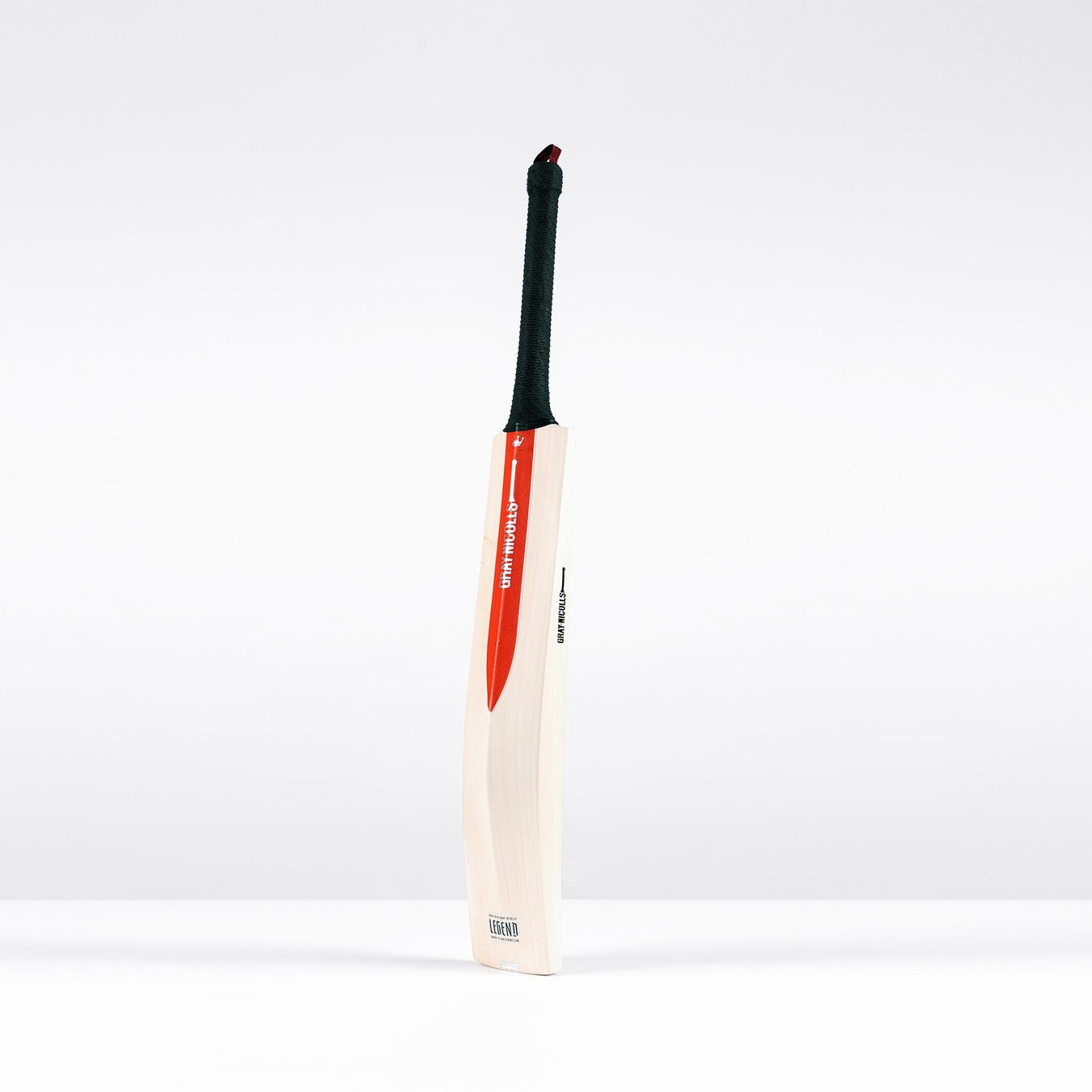 The Gray Nicolls Legend Silver Edition Junior Cricket Bat, a wooden English willow bat with a black handle and red and white sticker, featuring an expanded sweet spot, stands upright against a plain white background.
