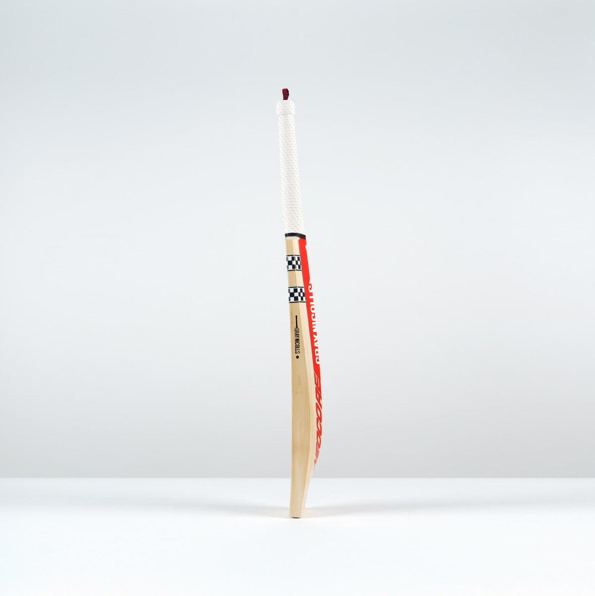 The Gray Nicolls Neocore Pro SH Cricket Bat 2026, showcasing a white handle and checkered design with advanced NEOCORE technology, stands upright on a white surface against a plain, light gray background.